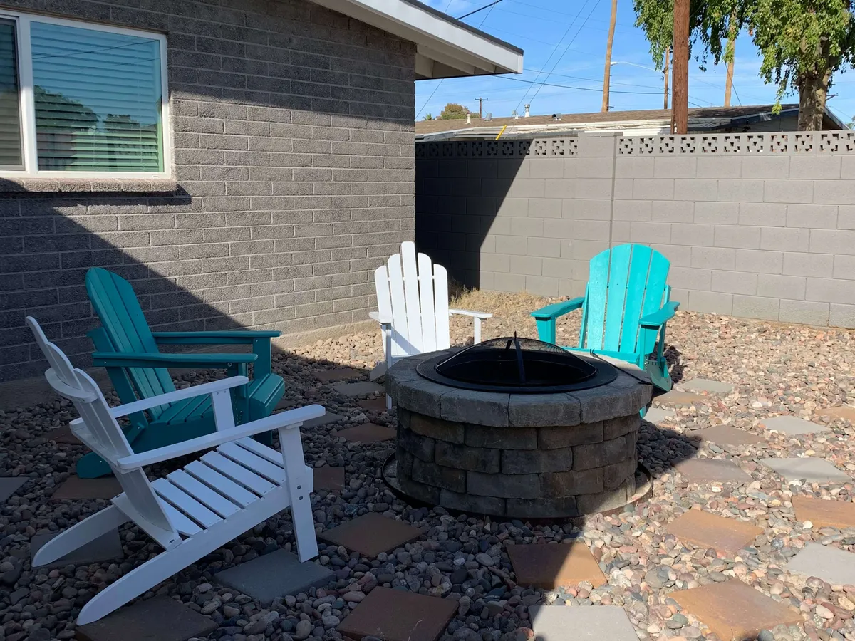 A cozy fire pit encircled by classic Adirondack chairs on a pebble-covered ground. The setup suggests intimate evening gatherings, with the warm glow inviting guests to unwind, share stories, or stargaze as the sun sets.