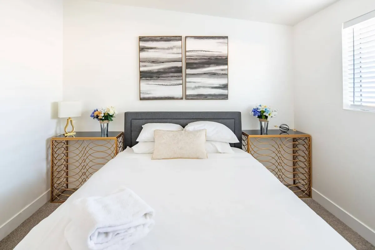 A cozy bedroom highlighted by a comfortable bed with decorative pillows and modern abstract wall art. The room is finished with stylish nightstands and soft lighting from bedside lamps, conveying a sense of warmth and relaxation. The space feels intimate, ideal for guests seeking a peaceful retreat.