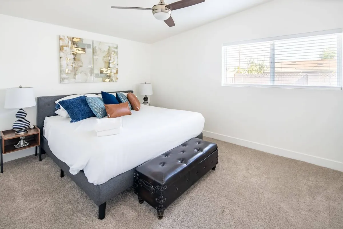 A beautifully styled bedroom featuring a plush bed adorned with soft, decorative pillows, tasteful artwork above the headboard, matching nightstands, and elegant light fixtures. Natural light filters through the windows, creating a serene and restful atmosphere ideal for relaxing or unwinding after a long day.