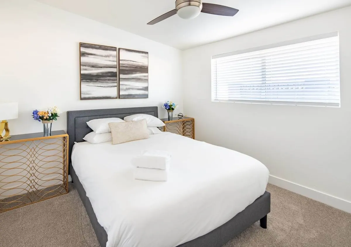 A serene bedroom featuring a neatly made bed, soft linens, and tranquil artwork above the headboard. The nightstand holds a reading lamp, creating an inviting atmosphere for relaxation after a day of outdoor activity.