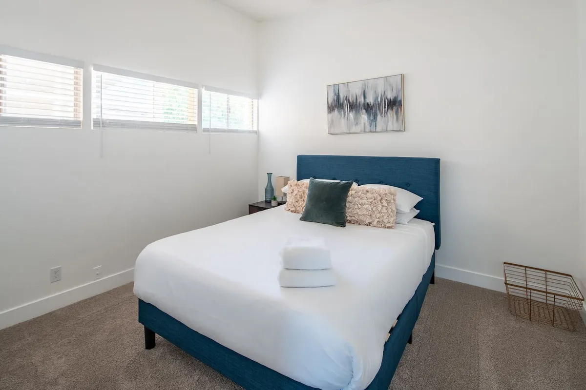 A cozy bedroom with a distinctive blue headboard, decorative pillows, and calming artwork. The nightstand and lamp add an extra touch of comfort, suggesting the space is ideal for both winding down and starting the day.