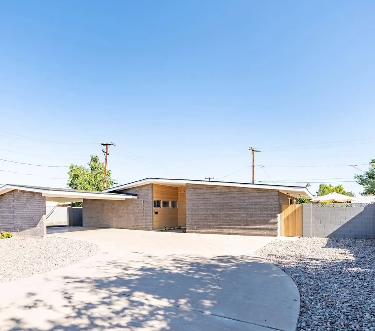 This image showcases the property's modern architectural exterior, featuring a landscaped driveway and a stylish wooden gate. The sunset lighting creates a welcoming ambiance, and the layout hints at ample outdoor space suitable for gatherings or relaxing after a day of adventure.