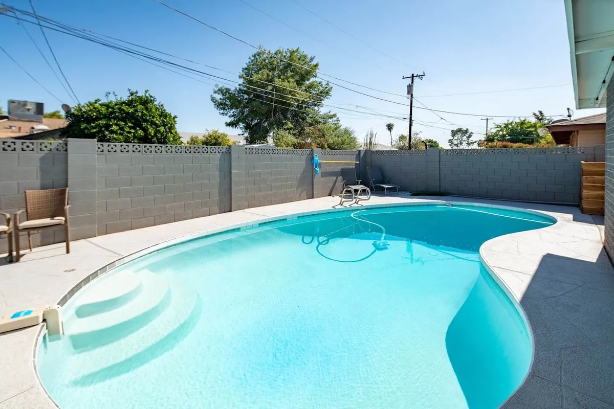 A sunlit view of a swimming pool, surrounded by a spacious patio. Lounge chairs and lush greenery line the area, providing plenty of space for sunbathing, relaxing, or entertaining guests in a tranquil environment.