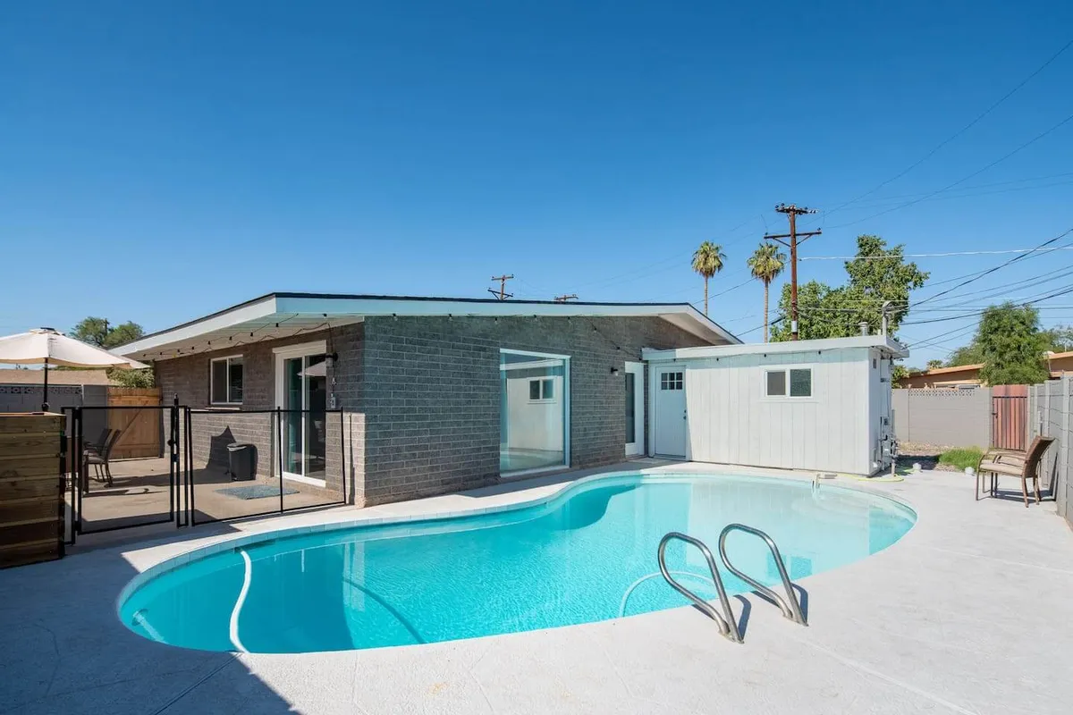 A wide-angle exterior shot featuring a sparkling swimming pool set against a modern house. The pool is flanked by a comfortable outdoor seating area, suggesting spaces for both swimming and relaxing. The scene is bright and refreshing, evoking a sense of resort-like tranquility.