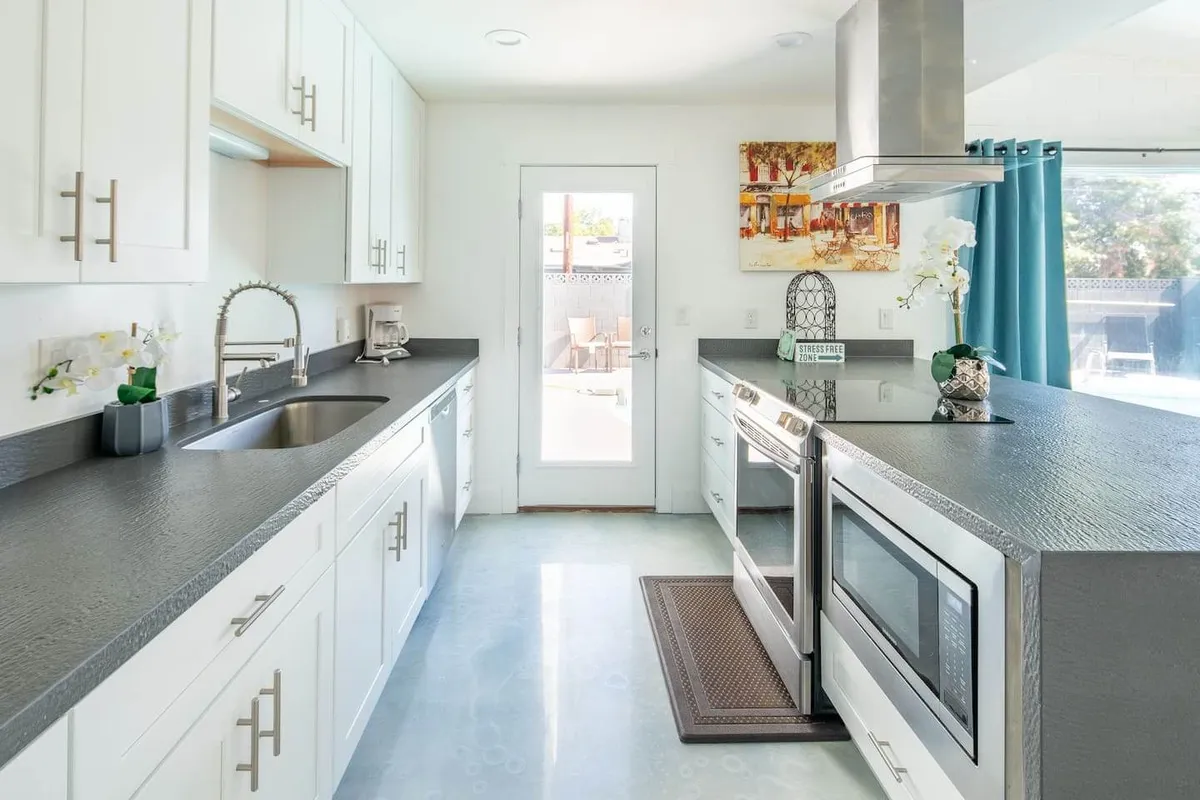 A modern kitchen featuring stainless steel appliances, a sleek island with a contemporary sink and faucet, and decorative artwork. The space is bright and inviting, with a door leading outside and thoughtful touches that highlight the kitchen's functionality and style.